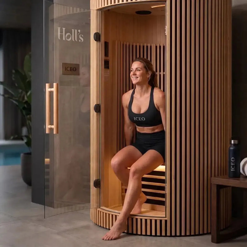 Vrouw zit in de ICEO Maan infraroodsauna voor 1 persoon met geopende glazen deur in een woonruimte