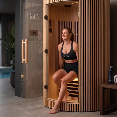 Vrouw zit in de ICEO Maan infraroodsauna voor 1 persoon met geopende glazen deur in een woonruimte
